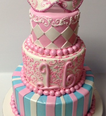 Pink With Mask Three Tier Fondant Sweet 16 With Mask Topper.Each Tier With Different Pattern.Stripes On The Lower Base Tier,Followed By Hand Scroll Work And A Whimsical Styled 16.Diamond Pattern Topper Cake With A Mask You May Also Like &#160;